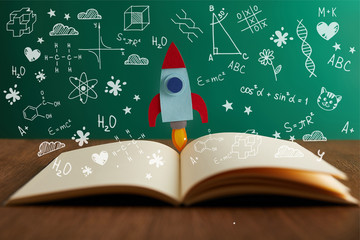 open book with colorful rocket on wooden table with math icons