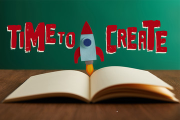 open book with colorful rocket on wooden table with universe icons