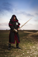 Knight with a sword in the hood against the background of the evening sky