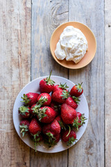 top view of a strawberry in a plate and whipped cream in a saucer on a wooden table