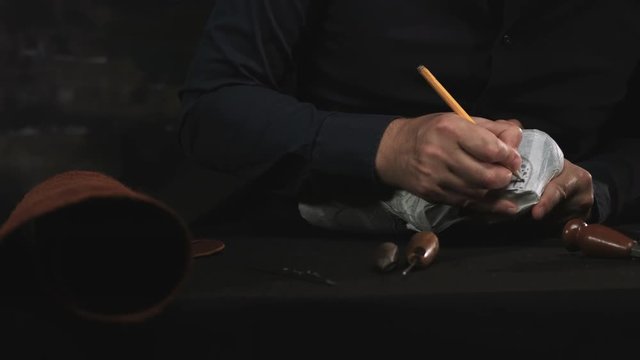 Close up of a male cobbler working with a blank for the shoe in workshop. Draws design shoes
