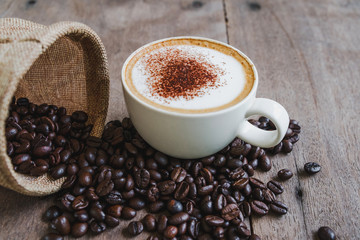 Coffee beans in the sack with a coffee cup on wooden table background.