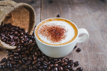 Coffee beans in the sack with a coffee cup on wooden table background.