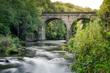 Fototapeta na wymiar Long exposure of waterfall on Derwent River underneath viaduct bridge