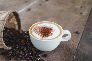 Coffee beans in the sack with a coffee cup on wooden table background.