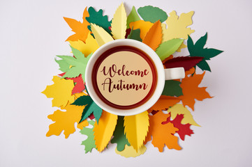 top view of cup of tea with "welcome autumn" lettering on colorful handcrafted leaves on white surface
