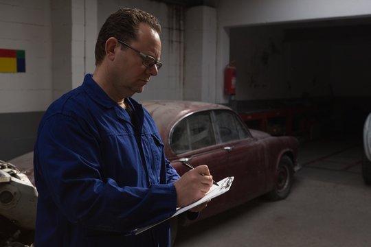 Male mechanic writing on clipboard