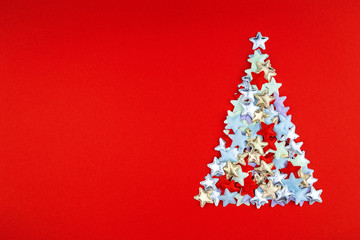 Fototapeta na wymiar Christmas tree of colored small stars on bright red background in flat lay style