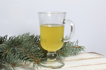 Blue spruce branches on a wooden box of boards, painted in white. Nearby is a glass of yellow liquor.