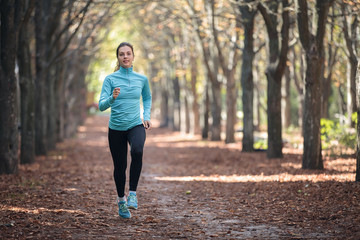 Athletic young woman runs in sportswear in the park in the fall.