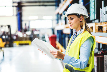 A portrait of an industrial woman engineer in a factory holding paperwork.