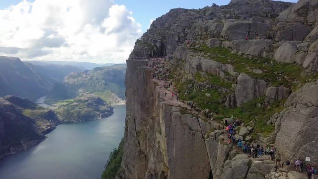 Tracking aerial shot of the Preikestolen hike, with lots of people moving. Lysefjord can be seen in the background.