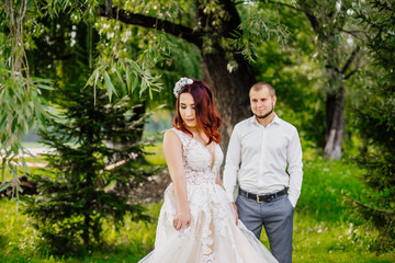Bride and groom in a park kissing. Young wedding couple newlyweds bride and groom at a wedding in nature green park near lake. Walking and kissing photo portrait. Before wedding ceremony.