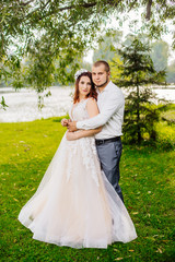 Bride and groom in a park kissing. Young wedding couple newlyweds bride and groom at a wedding in nature green park near lake. Walking and kissing photo portrait. Before wedding ceremony.