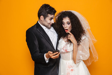 Photo of excited zombie couple bridegroom and bride wearing wedding outfit and halloween makeup...
