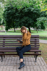 Fototapeta premium Beautiful girl is sitting on a bench with a tablet in the park.