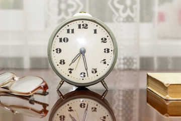 old metal alarm clock, glasses, a book on a polished table with