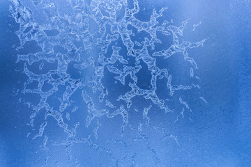 Fancy drawing of ice crystals on blue frozen winter window. 