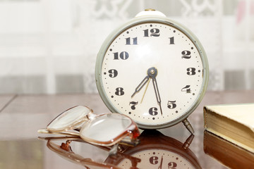 Naklejka premium old metal alarm clock, glasses, a book on the table near the win