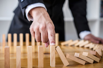 Wooden game strategy, Businessman hand stopping falling wooden dominoes effect from continuous toppled or risk, strategy and successful intervention concept for business