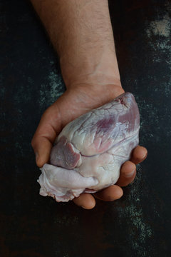 Heart in man's hand before cooking on black background. Raw meat. Offal
