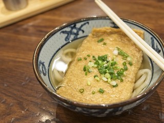 Ramen or Japanese noodles topping with deep fried tofu and scallions in clear soup served in a bowl on brown wooden table