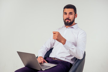 confident and handsome male office worker smiling and holding a laptop sitting on a chair on a white background in the studio full-length portrait