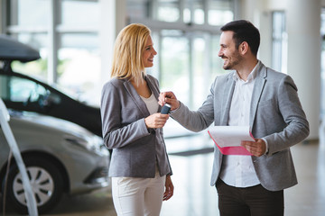 Woman is talking to handsome car dealership worker while choosing a car