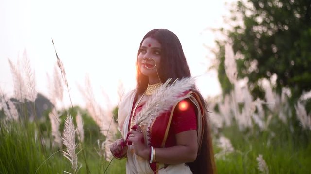 A beautiful and thoughtful Indian woman is happy and thinking about something in a calm way in a field at sunset or sunrise