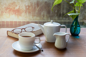 Cup of coffee and glasses on top of readbook on wood table.