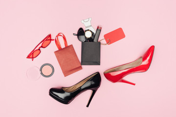 flat lay with high heels and little shopping bags with cosmetics and accessories isolated on pink