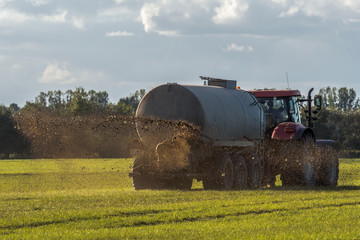 A farm tractor sprays its manure from the tanker onto a field. Manure is used as fertilizer in agriculture. Concept: agriculture