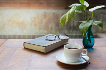 Cup of coffee and glasses on top of readbook on wood table.