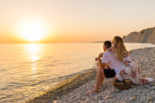 Young couple in love, man and woman enjoying romantic evening on the beach watching the sunset