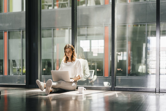 Businesswoman sitting on ground in empty office, using laptop