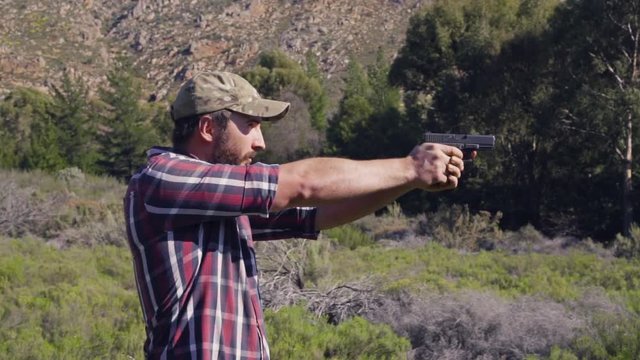 A man shooting a gun in nature outdoors