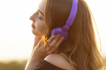 teenager girl in headphones listening to music on nature, young woman is relaxing in the summer field