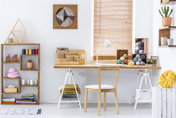 Real photo of a creative room interior with a desk, threads, knitting wool and graphic on a wall