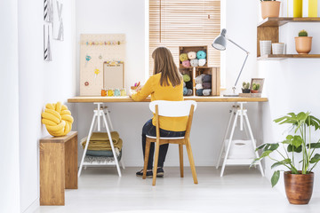 Woman sitting at a desk in a home office interior with knitting wool, organizer and yellow pillow - obrazy, fototapety, plakaty