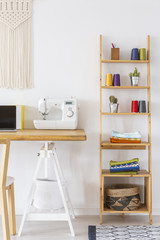 Real photo of a sewing machine on a desk next to a wooden shelf with colorful threads