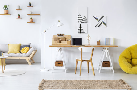 Real photo of a modern home office interior with graphics, desk, sofa and yellow pouf