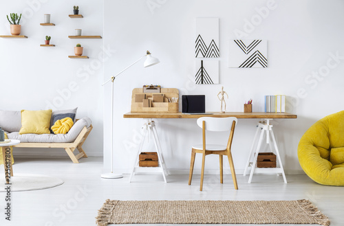 Real photo of a modern home office interior with graphics, desk, sofa and yellow pouf