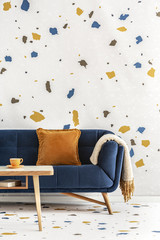 Wooden table in front of blue couch with orange pillow in colorful living room interior. Real photo