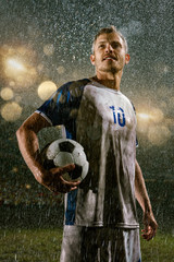 Soccer player on professional soccer night rain stadium. Dirty player in rain drops hold a football ball © Alex