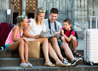 Family of four relaxing on old cathedral steps looking map