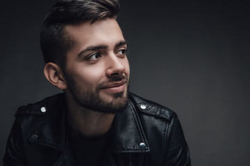 Attractive young man with a modern trendy hairstyle posing against a dark grey background with copyspace, head and shoulders portrait