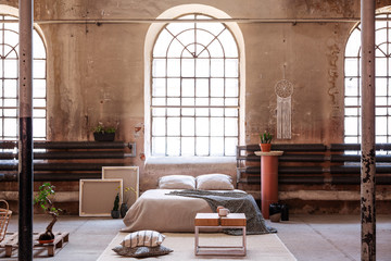 Table on rug in spacious bright bedroom interior with window above cushions on bed. Real photo