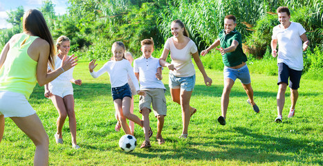 Parents with children gaily spending time together playing with ball outdoors