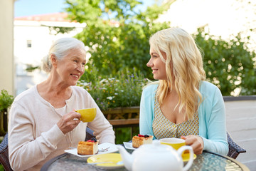 family, generation and people concept - happy smiling young daughter with senior mother drinking...