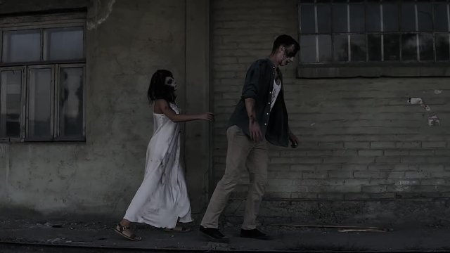 Halloween horror concept. Picture of creepy male and female ghost or zombie walking with wounded face. An old abandoned house on the background. Side view